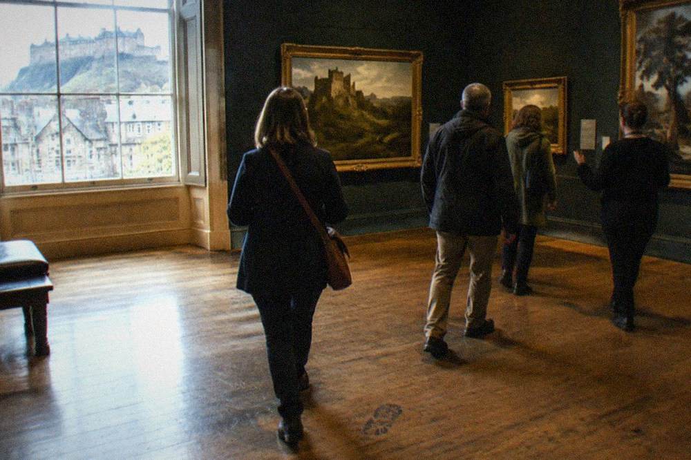 Gallery room with paintings hung on dark walls and wooden floorboards