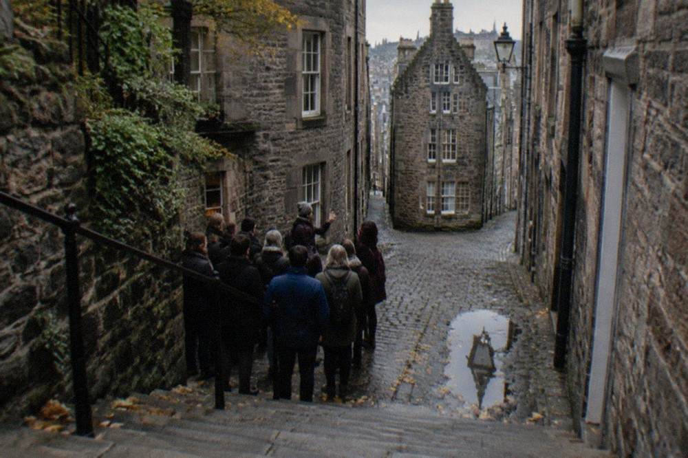 A tour group listening to a guide at the foot of a stone close in Edinburgh's Old Town