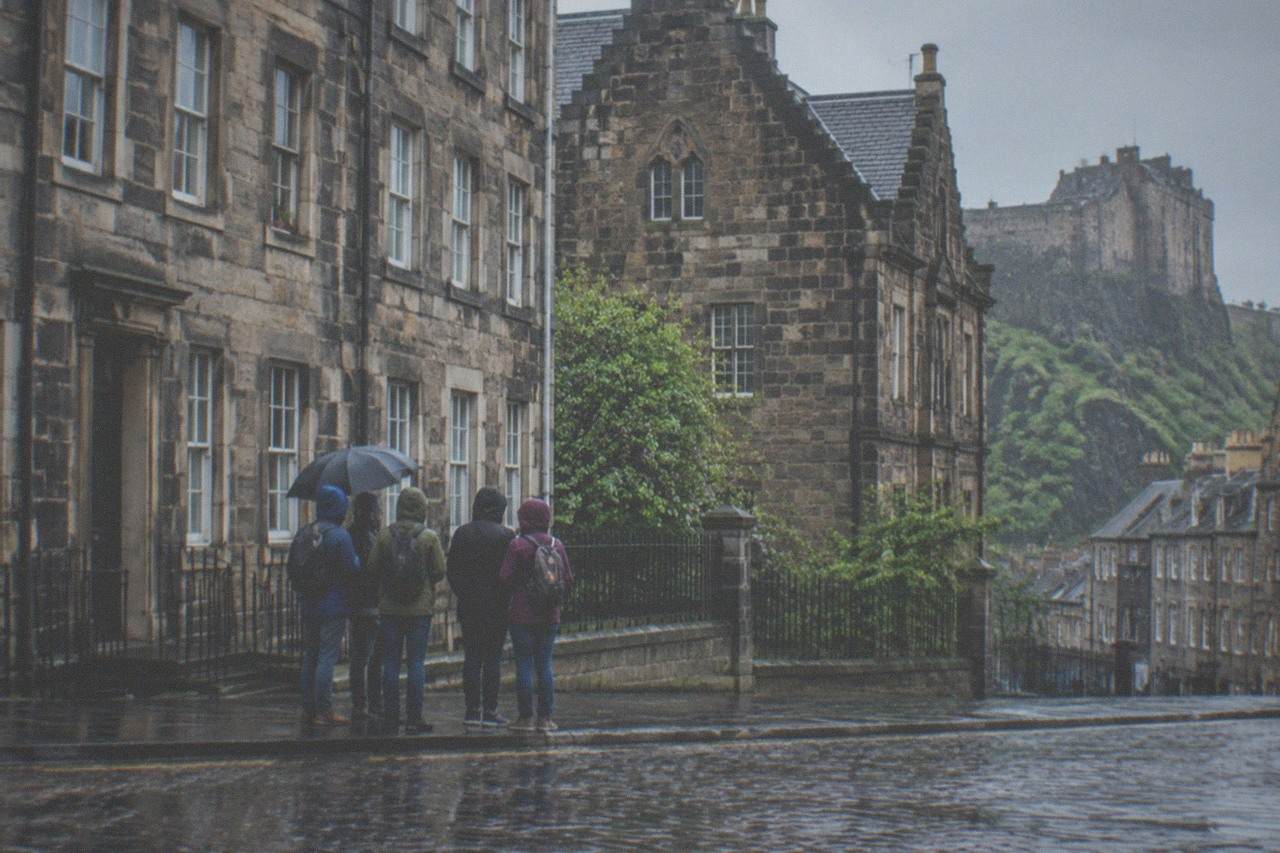 A guide speaking to a small group of visitors gathered on a cobbled Edinburgh street beside old stone buildings