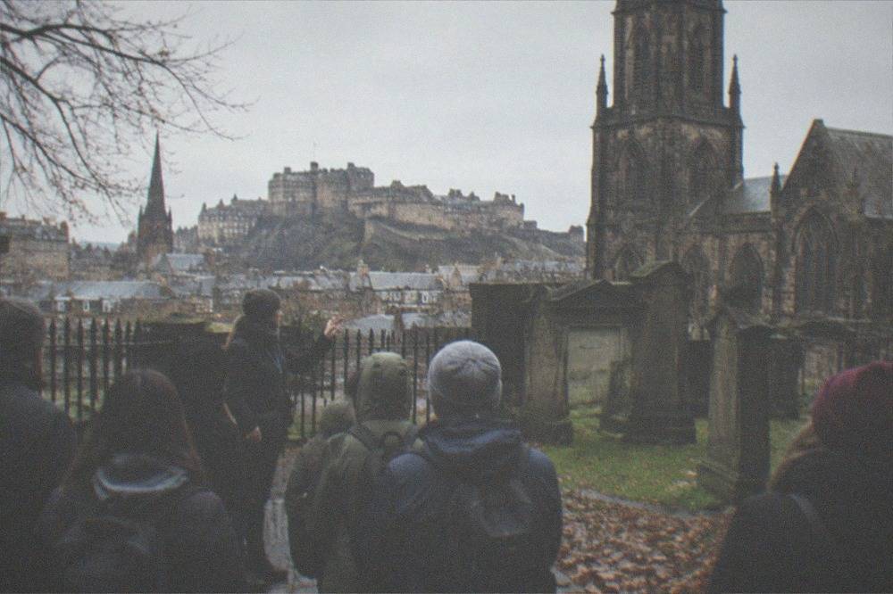 Old gravestones and a dark stone kirk tower behind a wrought iron fence