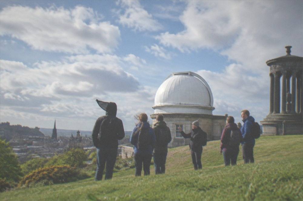 Hilltop observatory building with white dome beside a stone columned monument under a wide sky