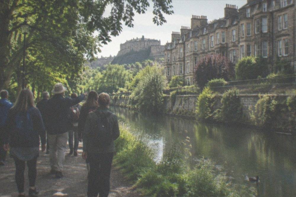 A riverside path beside stone buildings and a calm waterway lined with trees