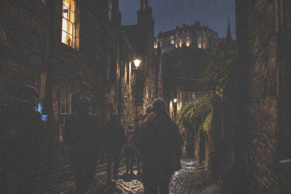 A dark stone wynd in the Old Town with warm light in an upper window