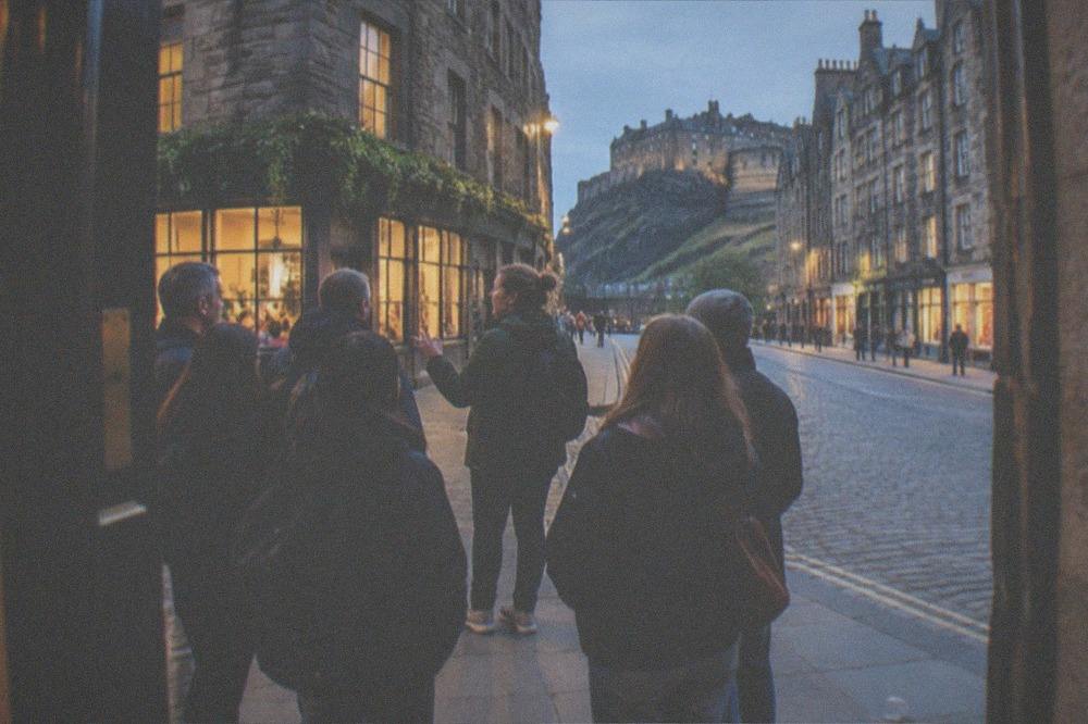 People walking along a lit Edinburgh street in the evening with warm shop lights