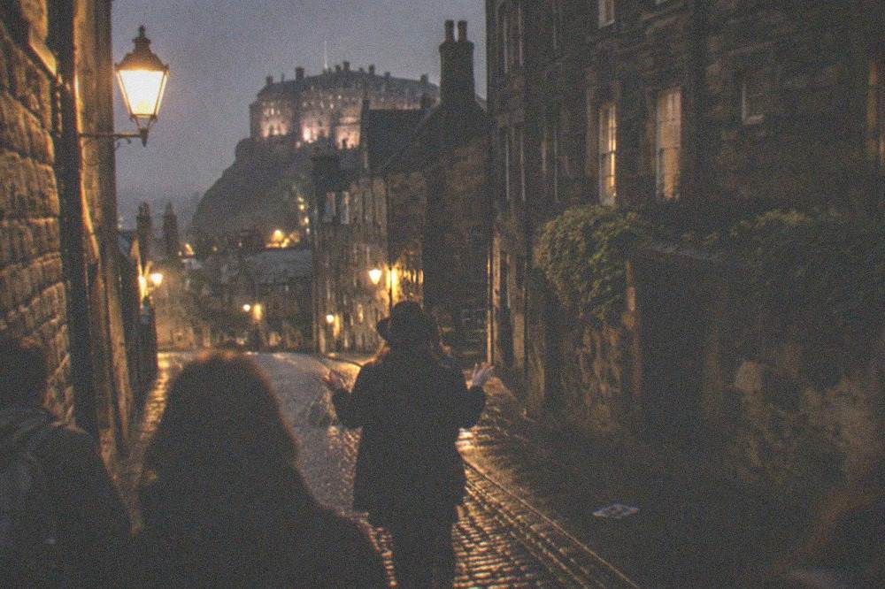 A candlelit close at night with dark stone walls and a narrow passage between buildings