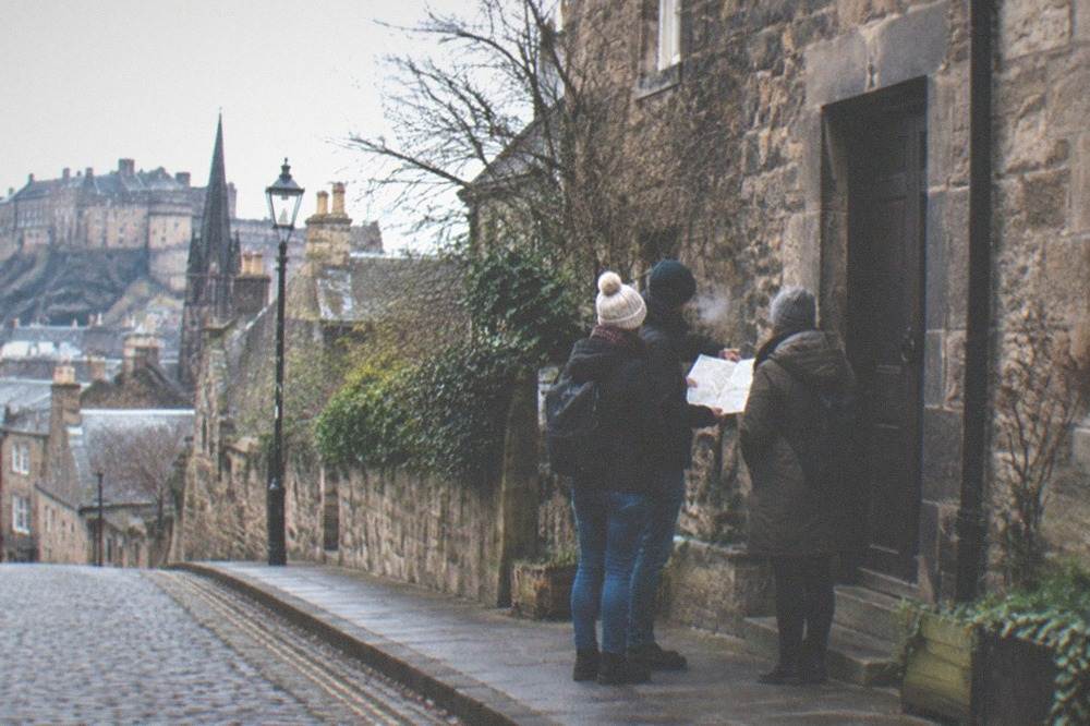 Visitors comparing a map outside a tour meeting point on the High Street in Edinburgh