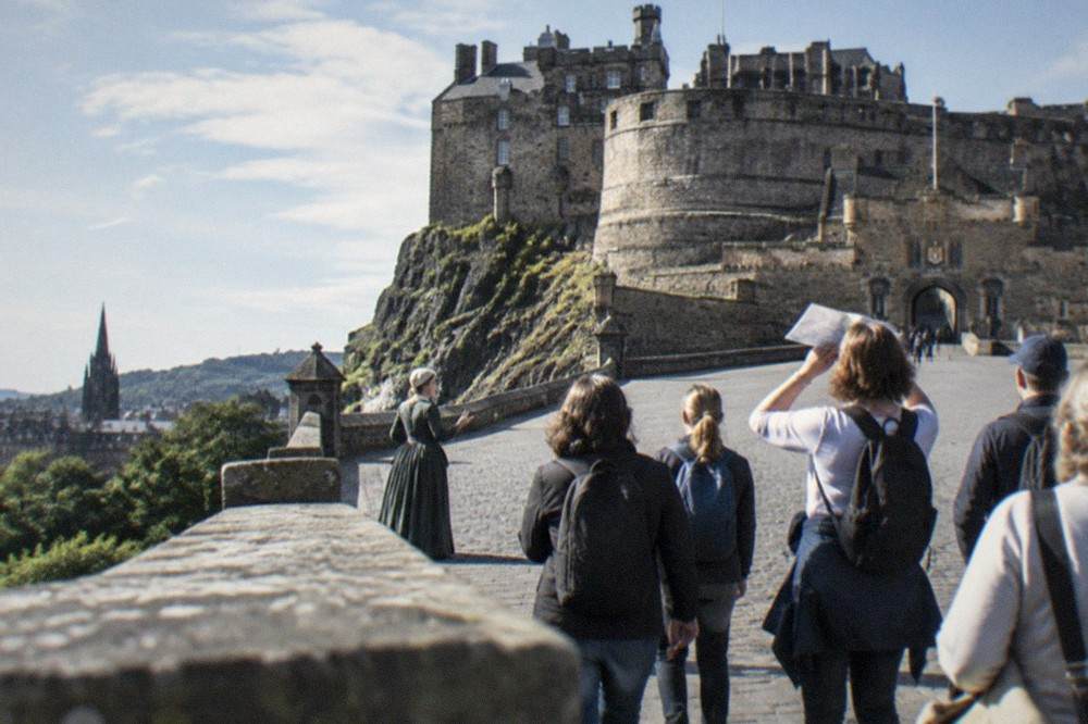 A guide in period costume addressing a small group below Edinburgh Castle's esplanade