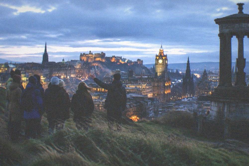Hilltop viewpoint at dusk overlooking a city skyline with a castle on a rocky ridge