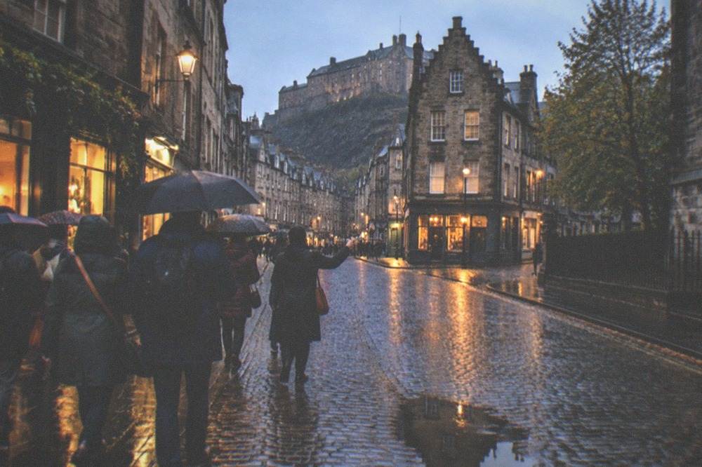 Wet cobbled street in Edinburgh's Old Town with rain-slicked stones reflecting shopfront light